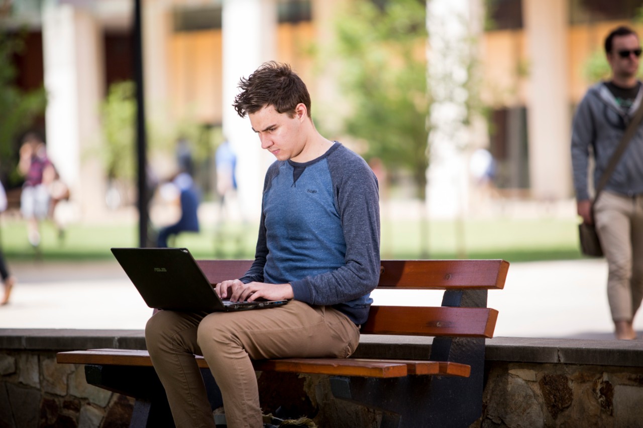 Student sitting on a bench with a laptop at the Barr Smith Lawns